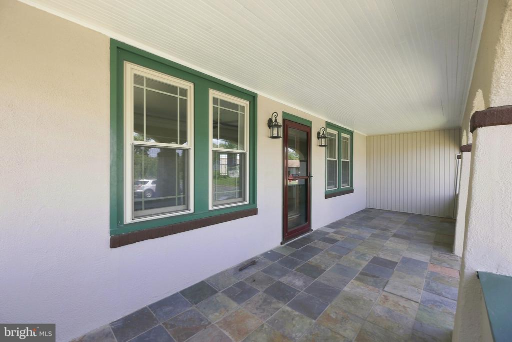 Covered front porch with green-trimmed windows and door, beadboard ceiling, and multicolored tile floor.