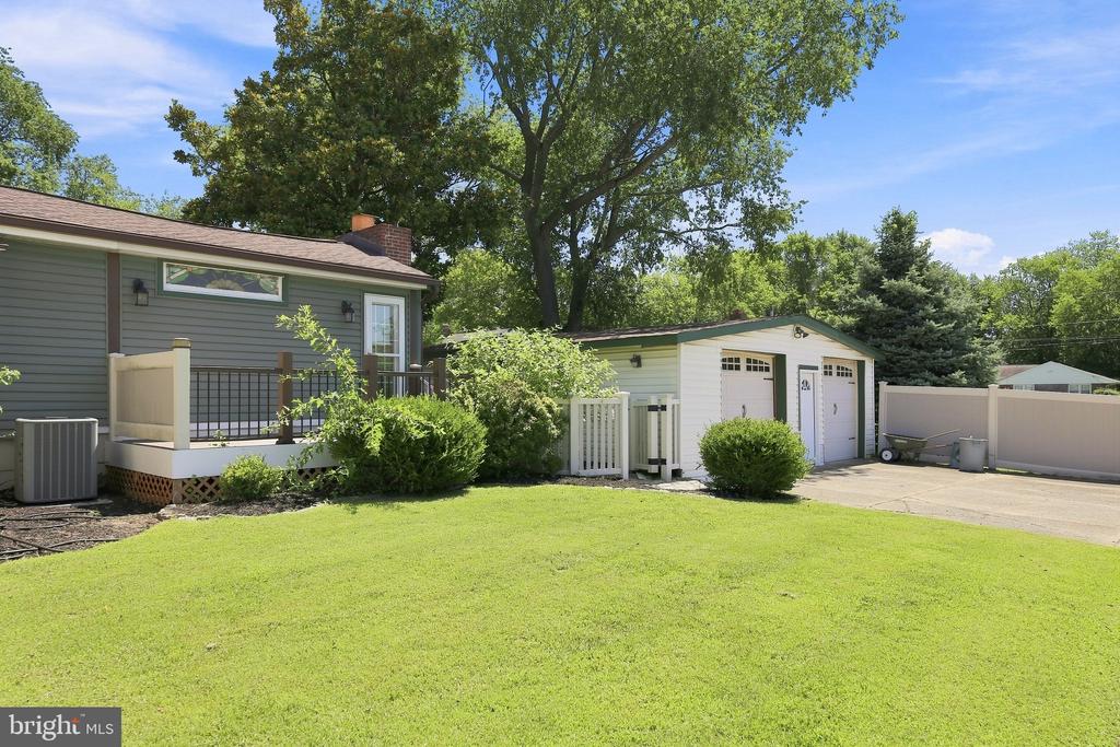 Home exterior with a detached white garage, broad lawn, and mature trees.