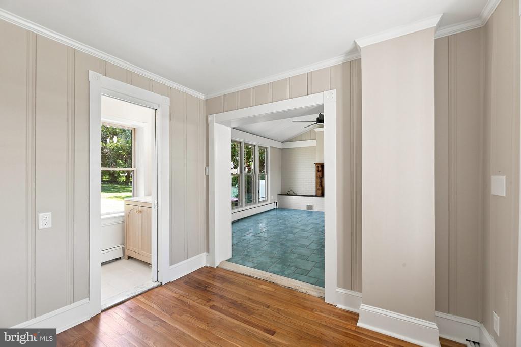 Hardwood-floored room with paneled walls and wide doorways to bright tiled spaces.