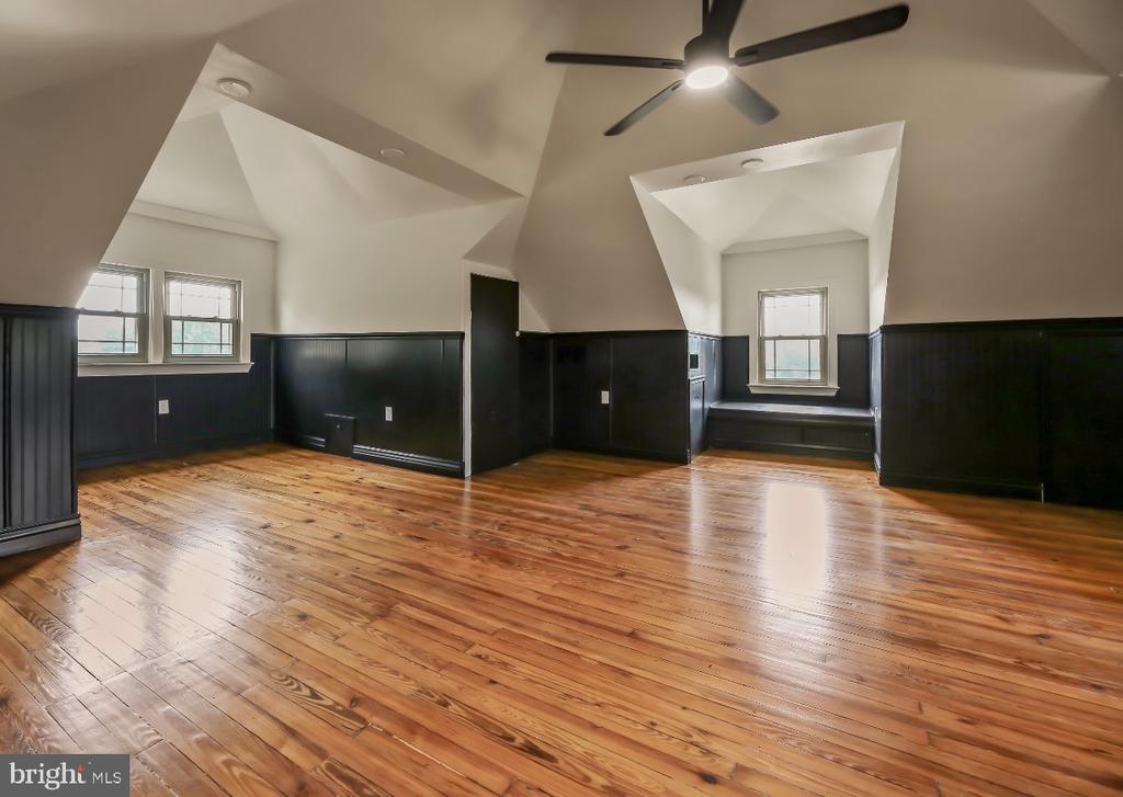 Spacious empty room with polished hardwood floors, dark wainscoting, vaulted ceiling, and ceiling fan.
