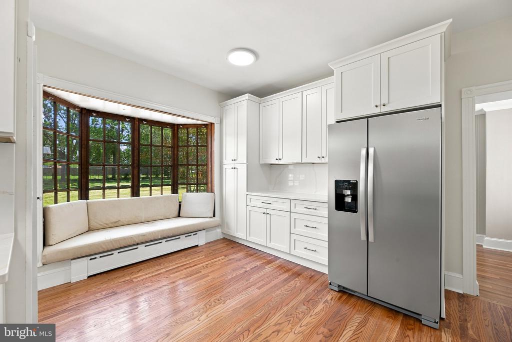 Bright kitchen with white cabinets, stainless steel refrigerator, wood floors, and a cushioned window seat.