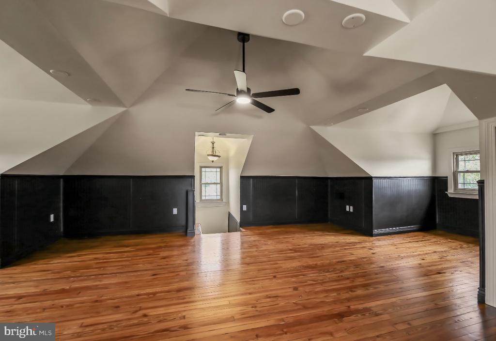 Vacant upstairs room with polished hardwood floors, dark paneling, and a high angular ceiling.