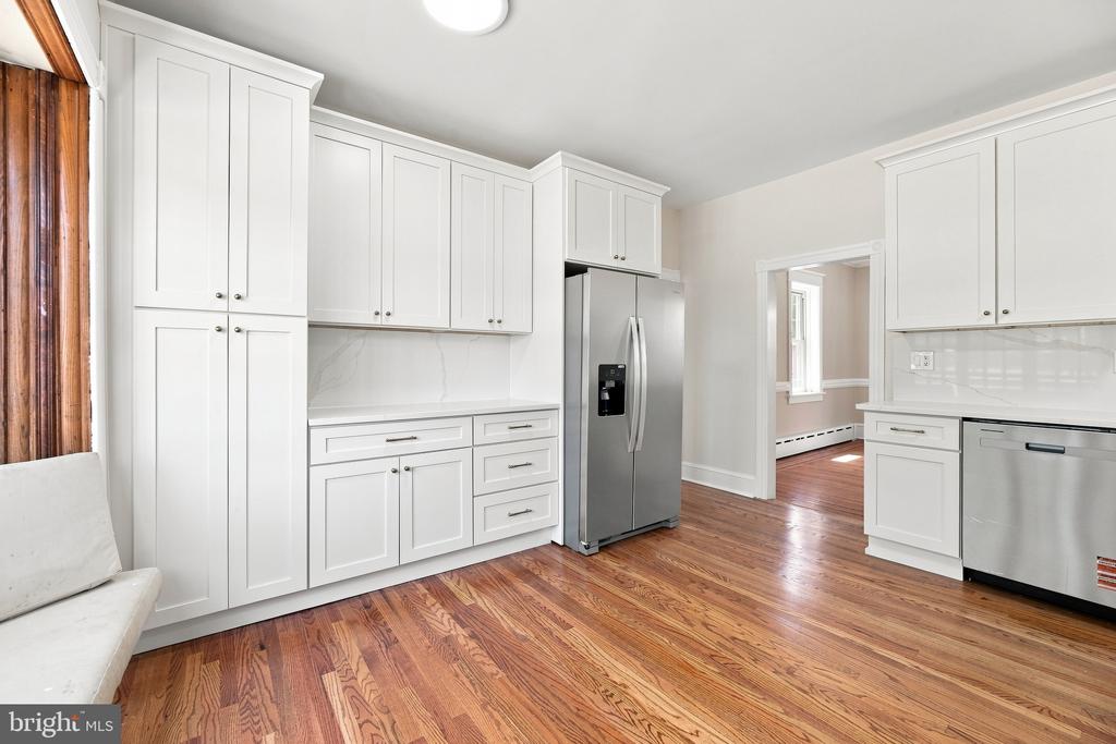 Kitchen with white shaker cabinets, stainless steel appliances, and polished reddish hardwood floors.