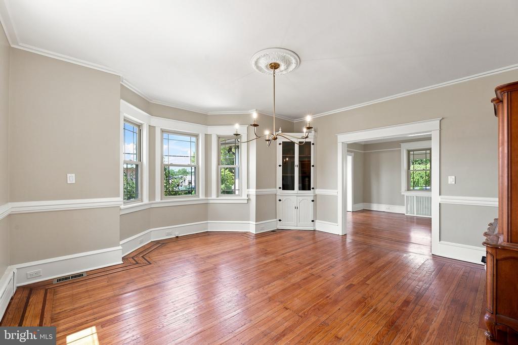 Vacant dining room with polished hardwood floors, bay windows, built-in cabinet, and chandelier.