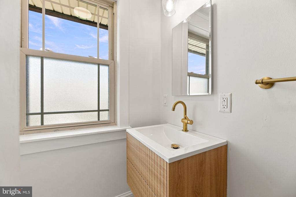Bathroom vanity with a white sink, brass faucet, and large window with frosted glass.