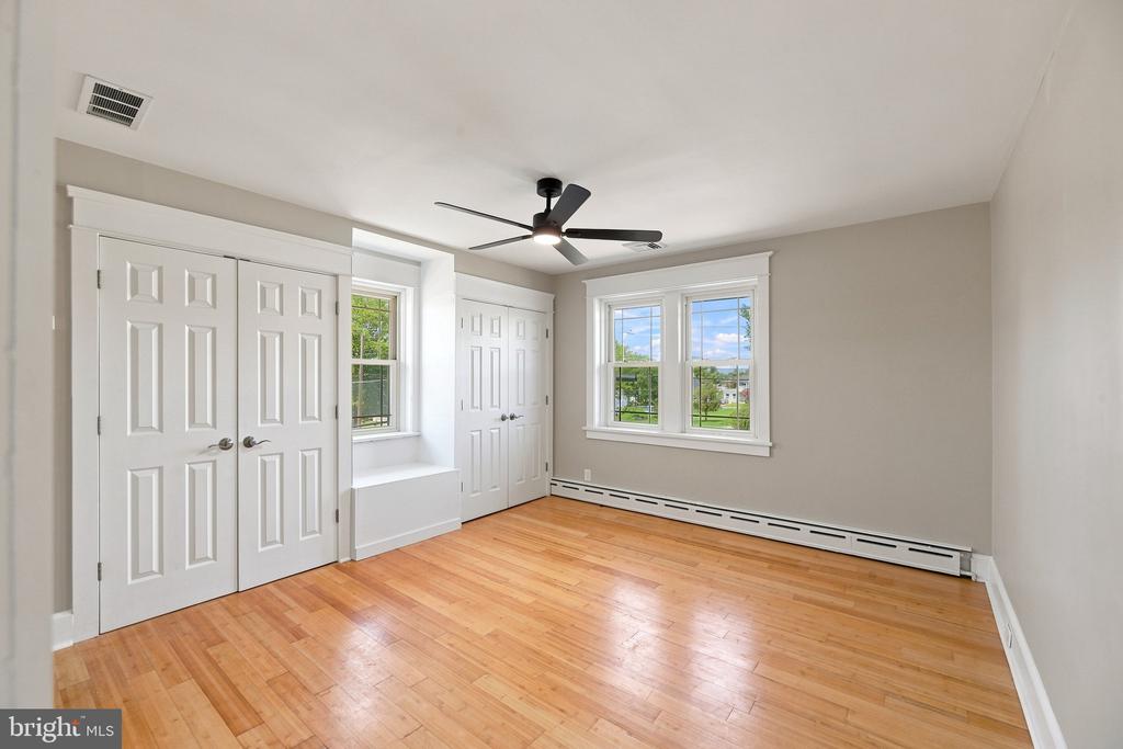 Vacant bedroom with hardwood floors, white closets, two windows, and a ceiling fan.