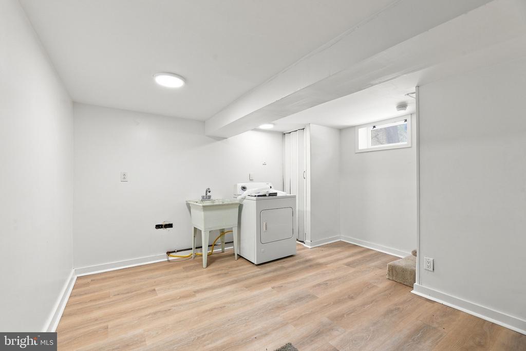 Laundry area with a utility sink, washer and dryer, and light wood-look flooring.