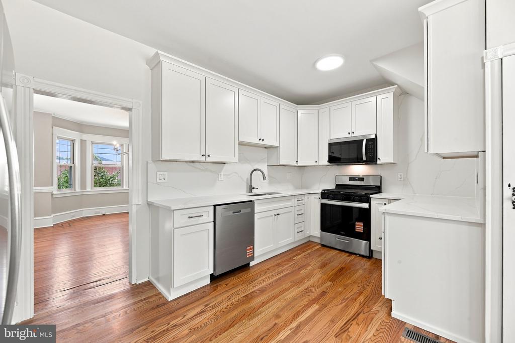 Kitchen with white cabinetry, stainless steel appliances, and warm hardwood floors.
