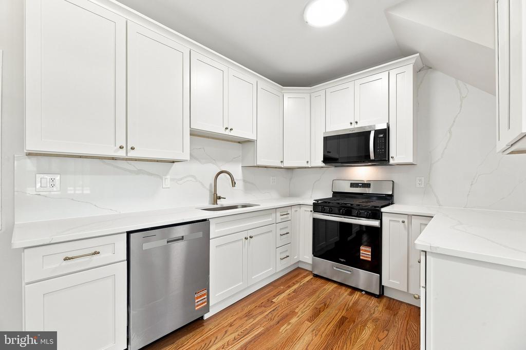 White kitchen with stainless steel appliances, marble-look counters, and warm hardwood floors.