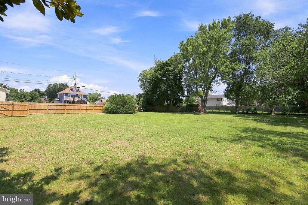 Residential backyard with a broad lawn, mature shade trees, and a wooden fence.