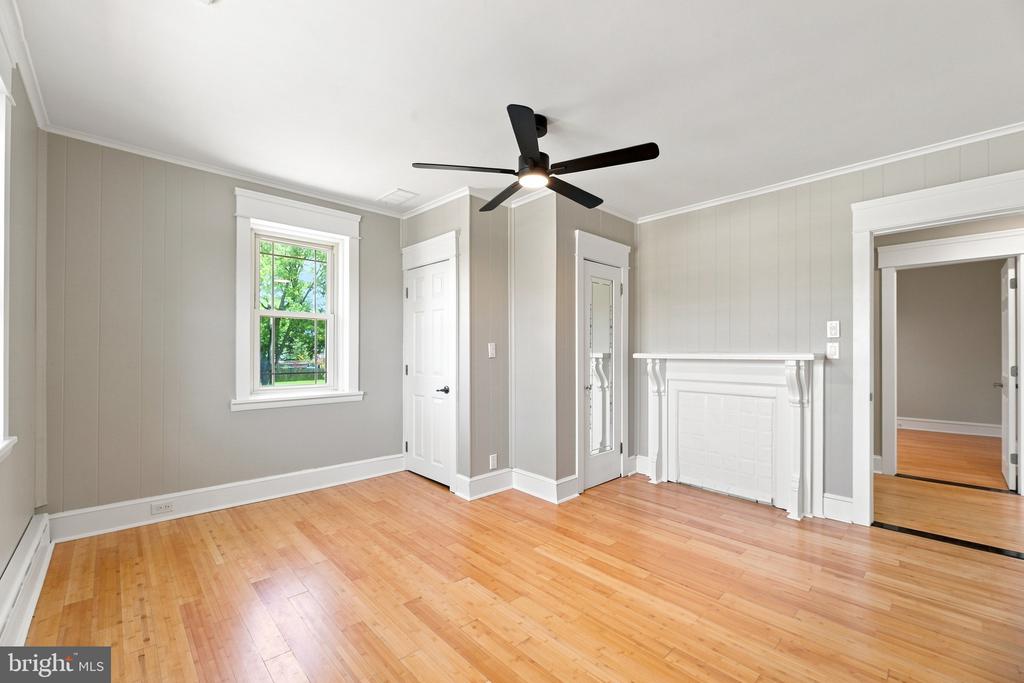 Empty room with hardwood floors, gray paneled walls, and a white fireplace.