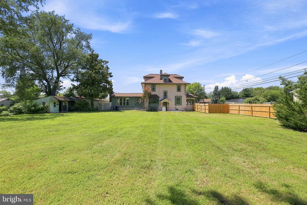 Rear of a two-story house beyond a broad lawn, with a wooden fence and mature trees.