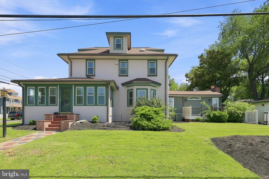 Two-story white house with green trim, enclosed porch, brick steps, and a broad front lawn.