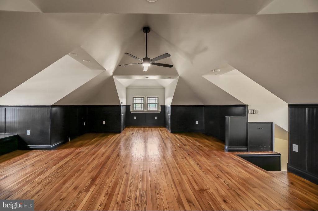 Vacant upper-level room with hardwood floors, sloped ceilings, dark paneling, and two far-end windows.