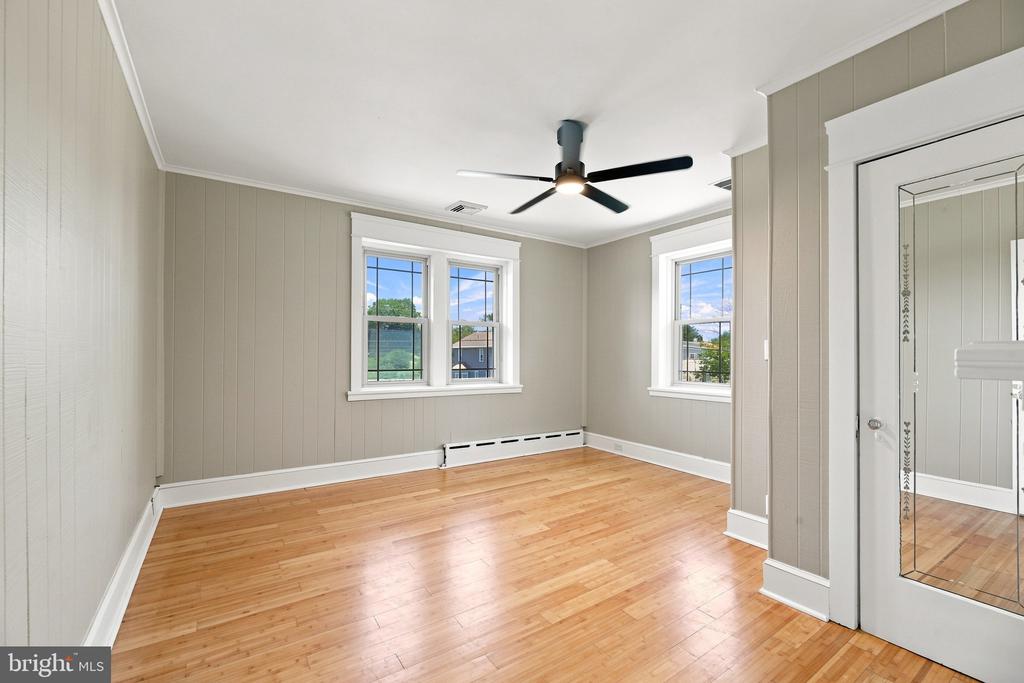 Vacant bedroom with hardwood floors, three windows, and mirrored closet doors.