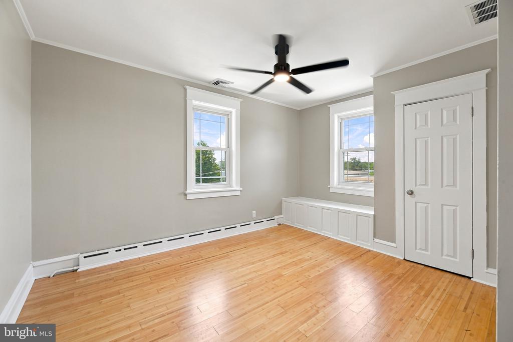 Empty bedroom with hardwood floors, two windows, a built-in window seat, and a ceiling fan.