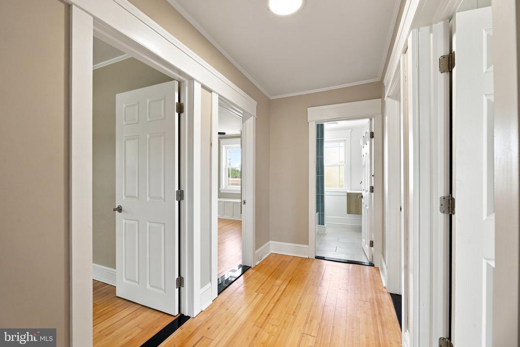 Empty hallway with hardwood floors, white paneled doors, and a tiled room at the far end.