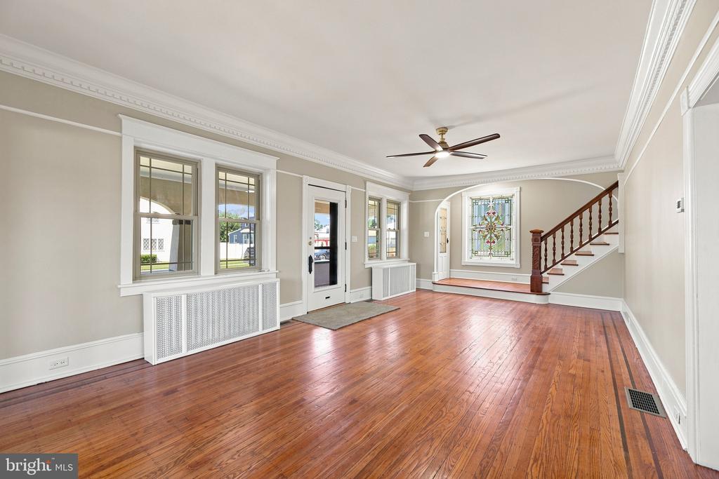 Vacant room with polished hardwood floors, a staircase, and a decorative stained-glass window.