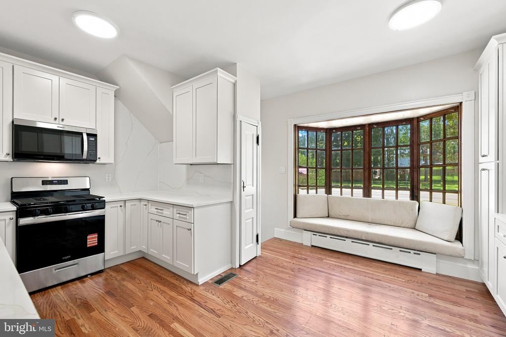 Kitchen with white cabinets, wood floors, and a cushioned window seat overlooking the yard.