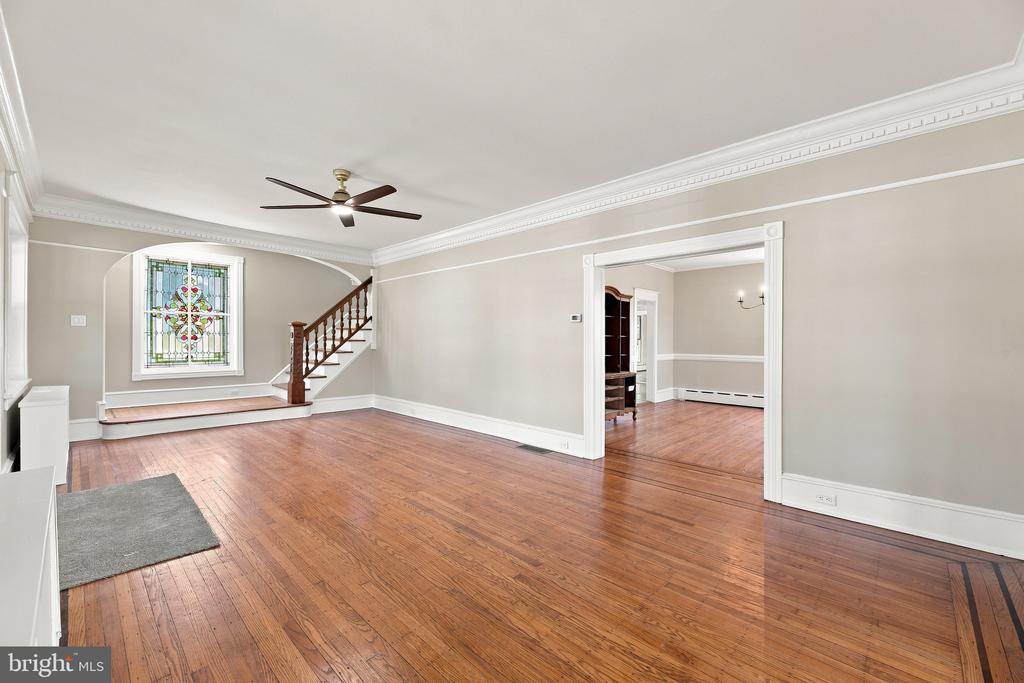 Empty living room with hardwood floors, a staircase, and a stained-glass window.