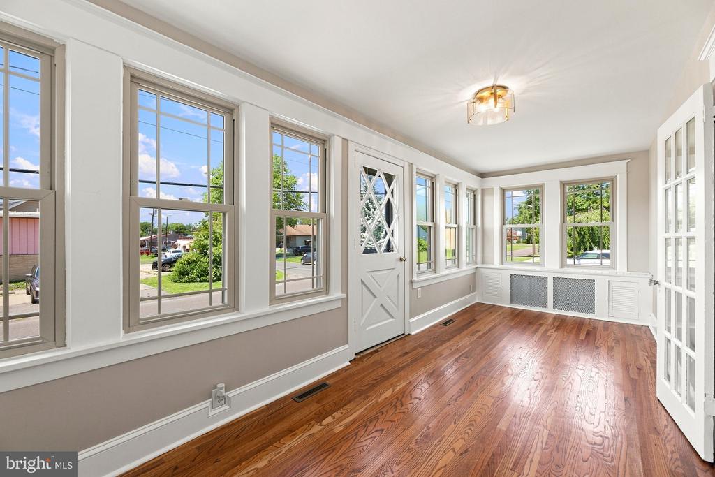 Vacant sunroom with hardwood floors, white trim, and windows on three sides.