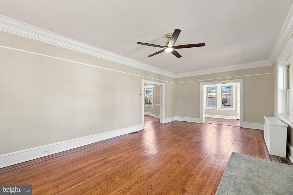 Unfurnished living room with hardwood floors, crown molding, a ceiling fan, and large windows.