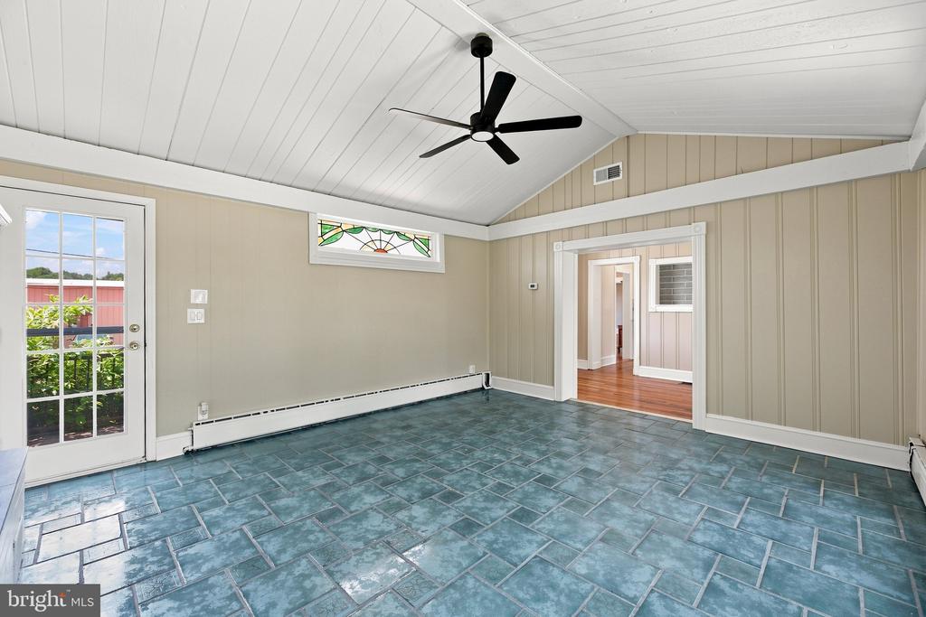 Empty sunroom with blue-green tile floors, vaulted ceiling, black fan, and glass-paned exterior door.