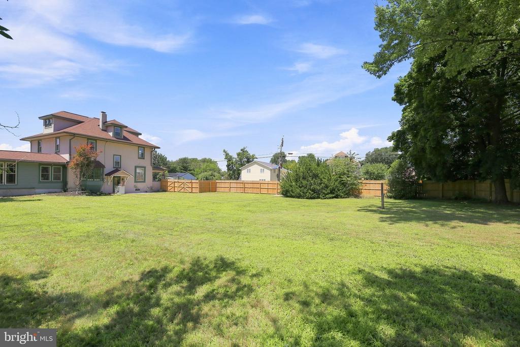 Large grassy backyard with wooden fencing, mature trees, and the house along the left side.