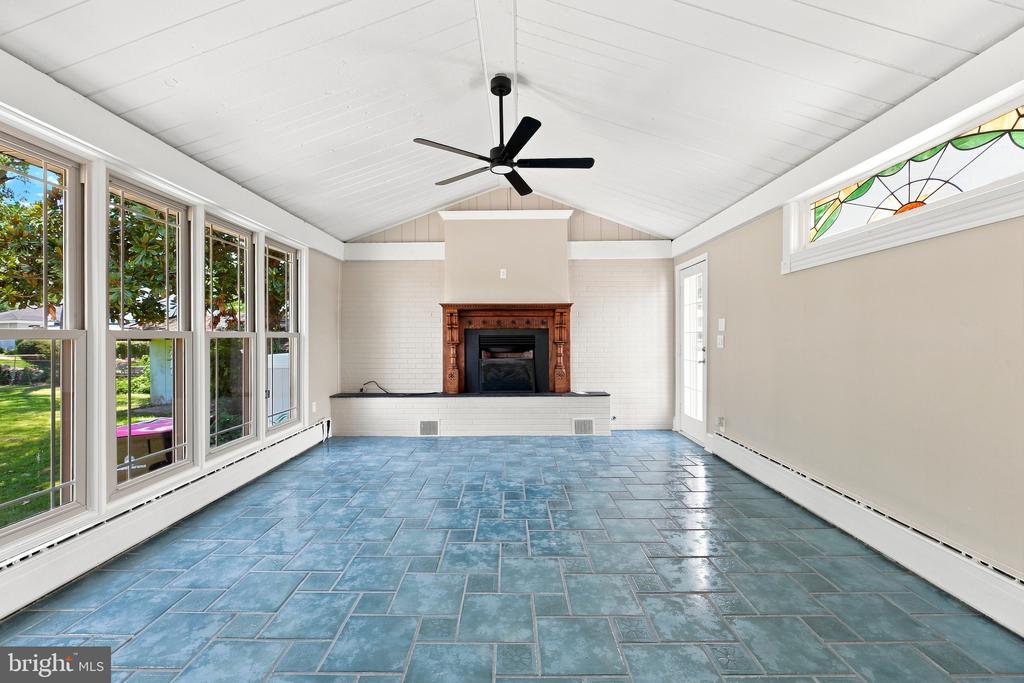 Vacant sunroom with blue tile floors, a fireplace, vaulted ceiling, and tall windows.
