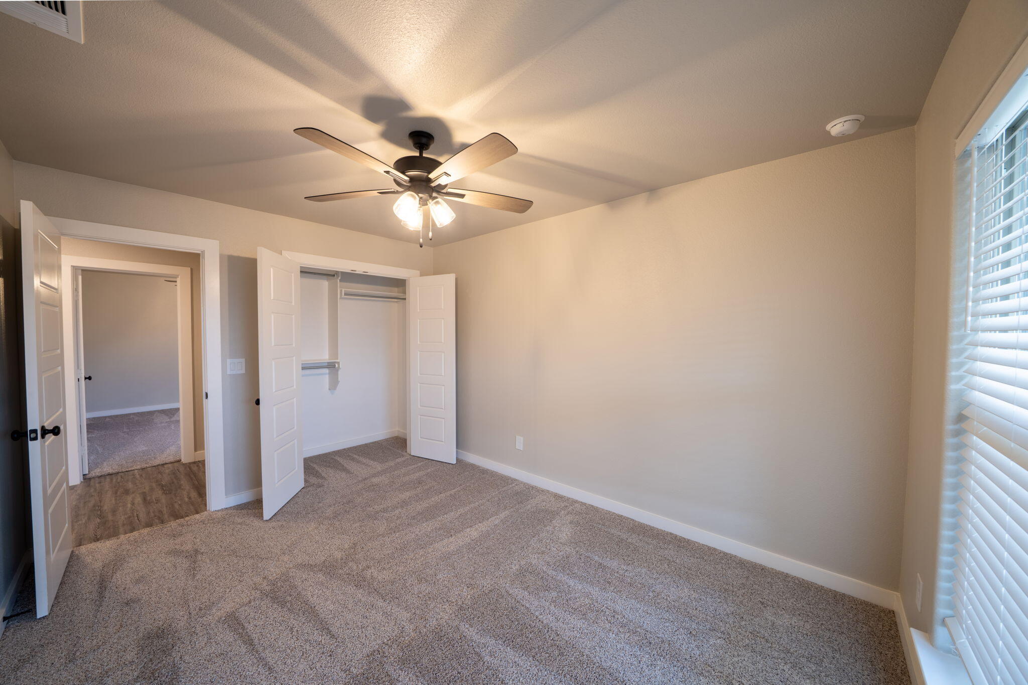 Empty carpeted bedroom with an open closet, ceiling fan, and window with blinds.