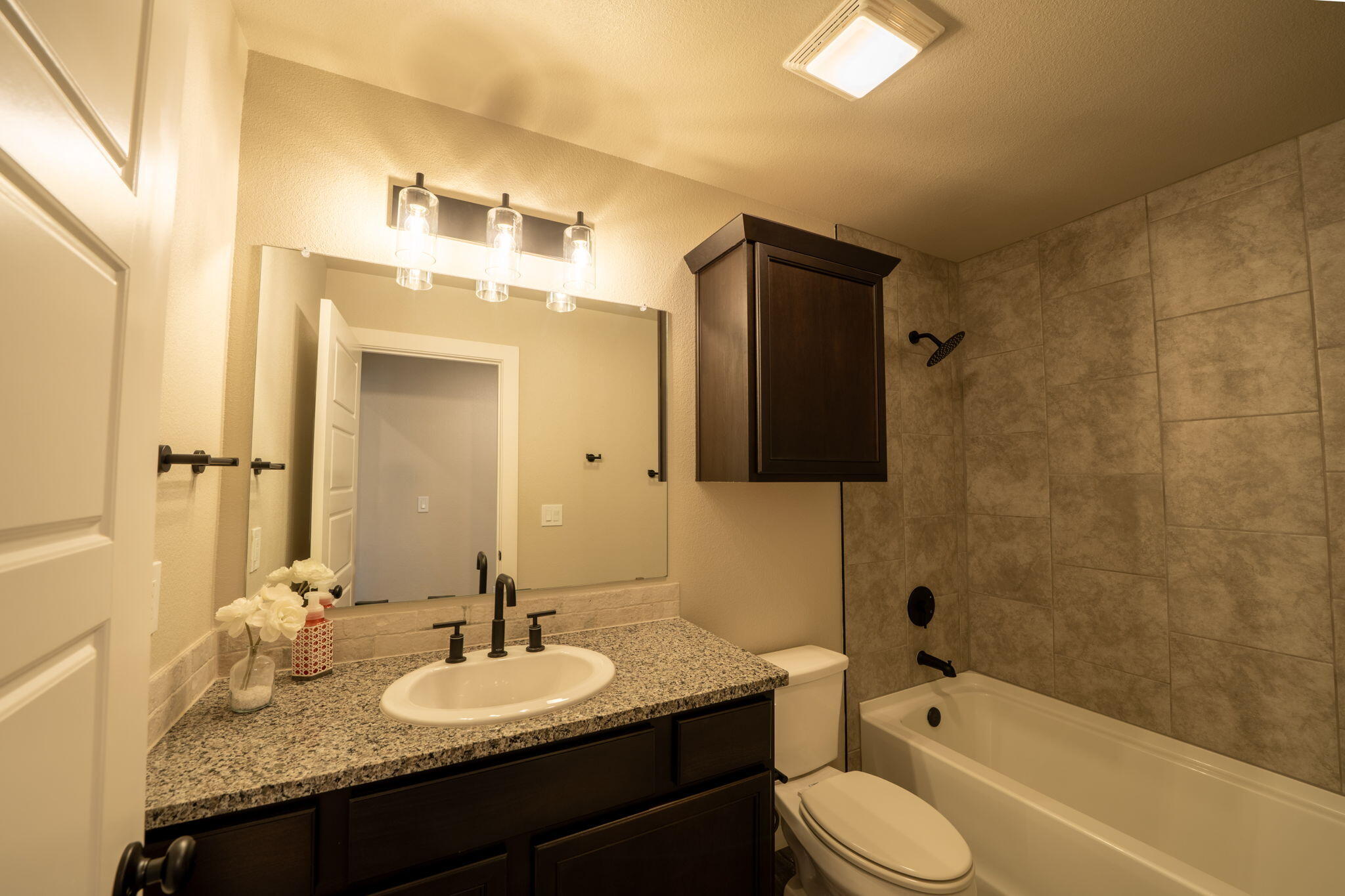 Bathroom with granite vanity, dark cabinets, and a beige tiled tub-shower surround.