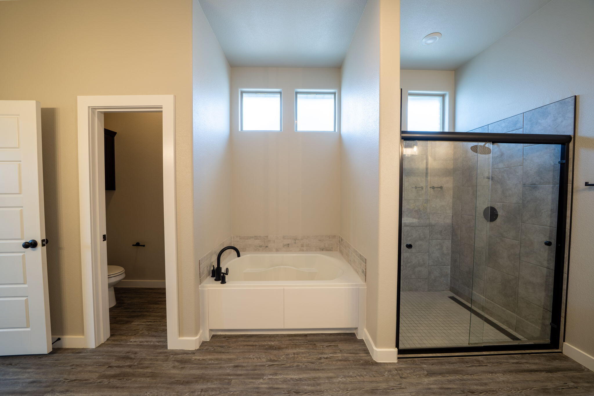 Primary bathroom with a soaking tub beneath two windows and a spacious glass-enclosed tiled shower.