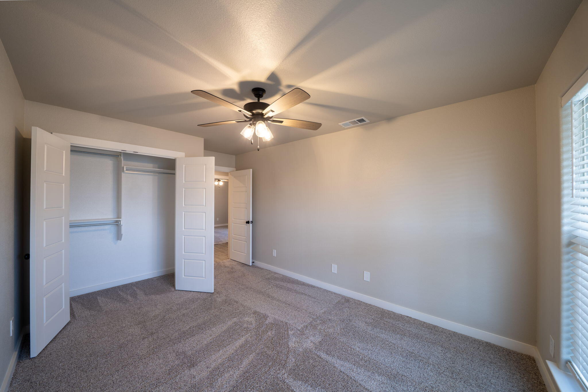 Empty bedroom with an open closet, ceiling fan, gray carpet, and window blinds.