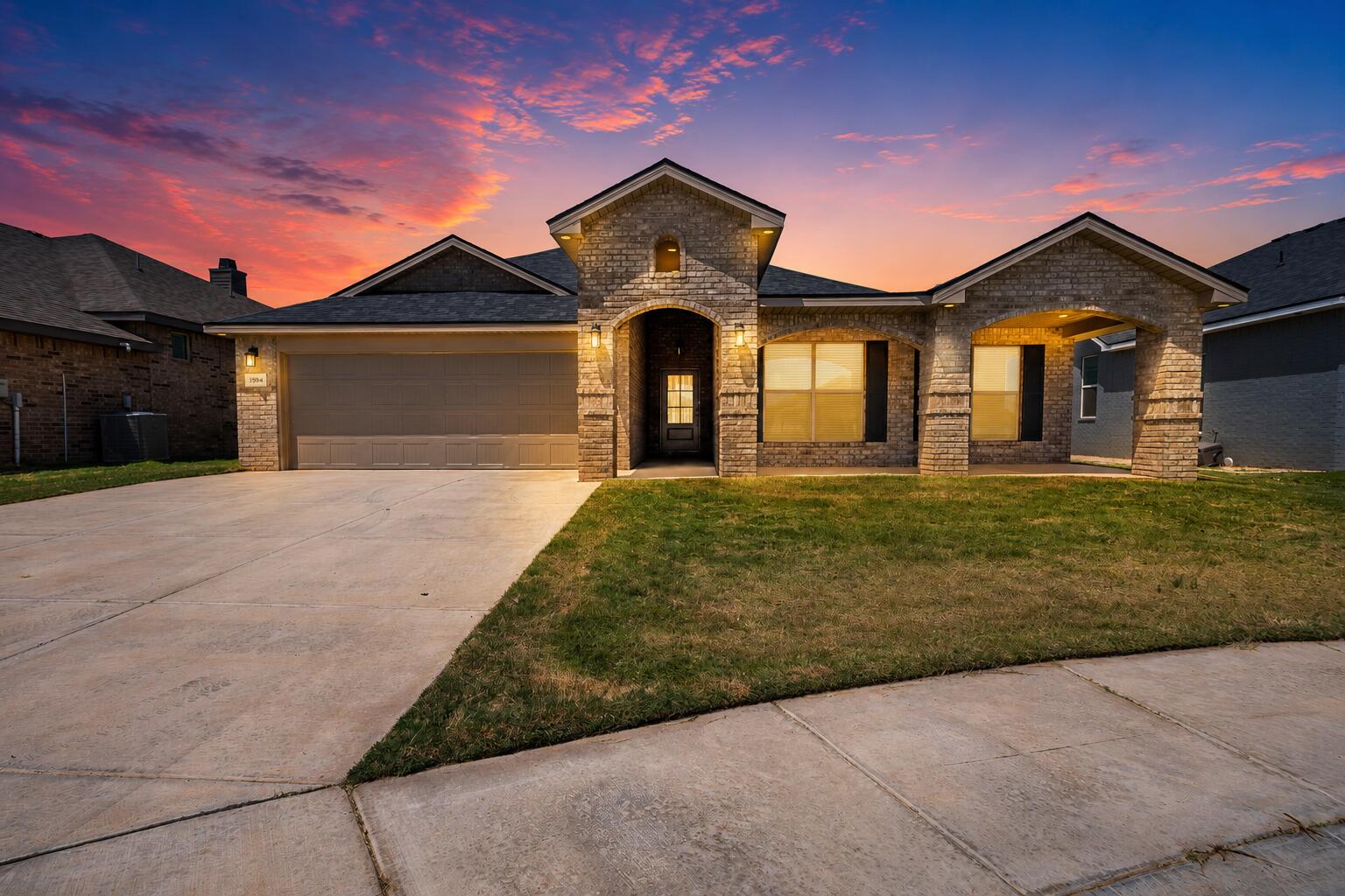 Brick house with a two-car garage and covered entry beneath a colorful sunset sky.