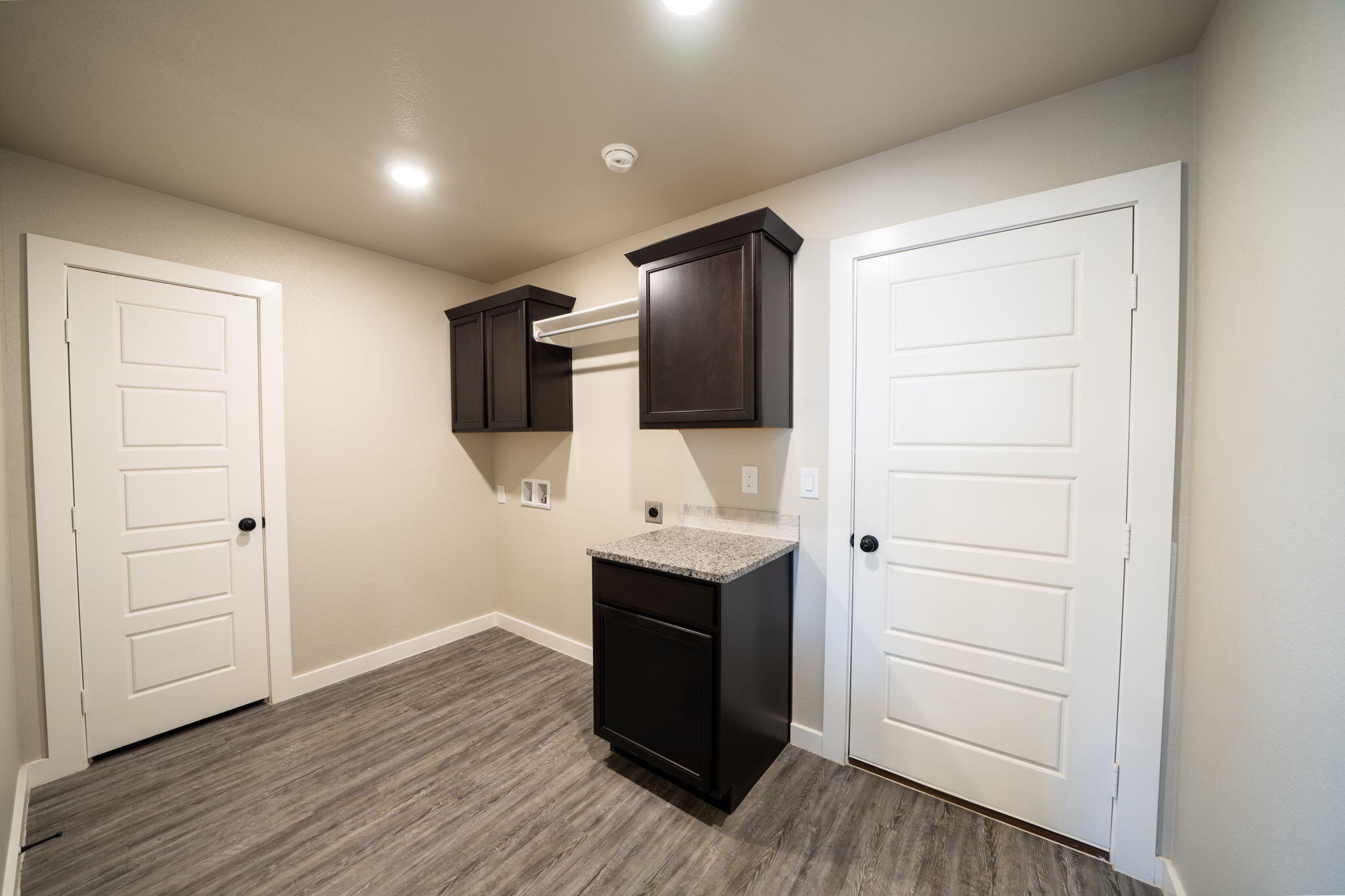 Laundry room with dark cabinets, granite counter, washer and dryer hookups, and gray wood-look flooring.