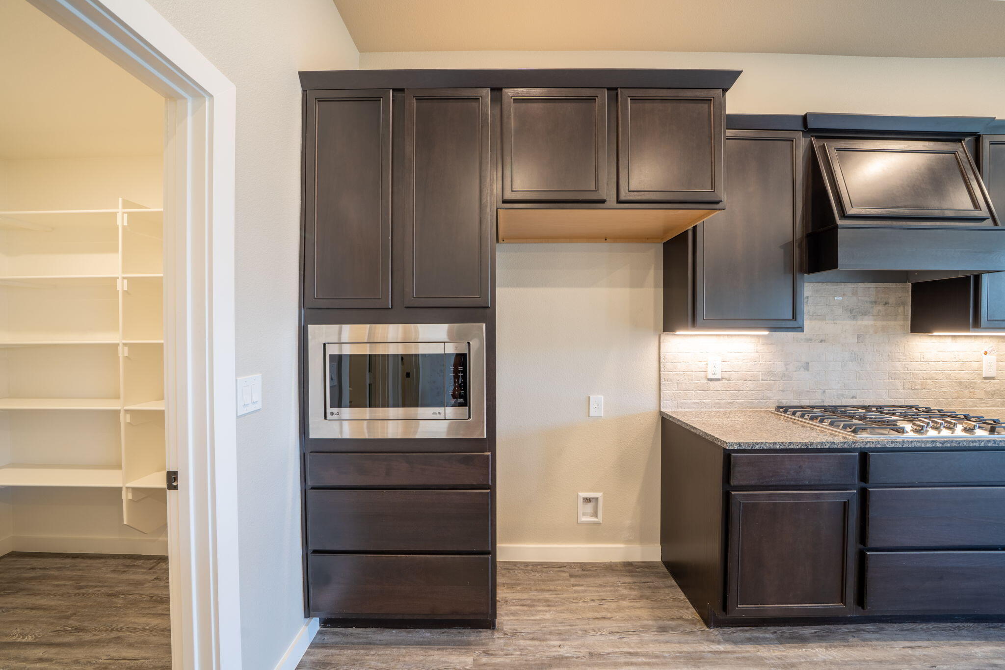 Kitchen with dark cabinets, built-in microwave, gas cooktop, and open pantry shelving.