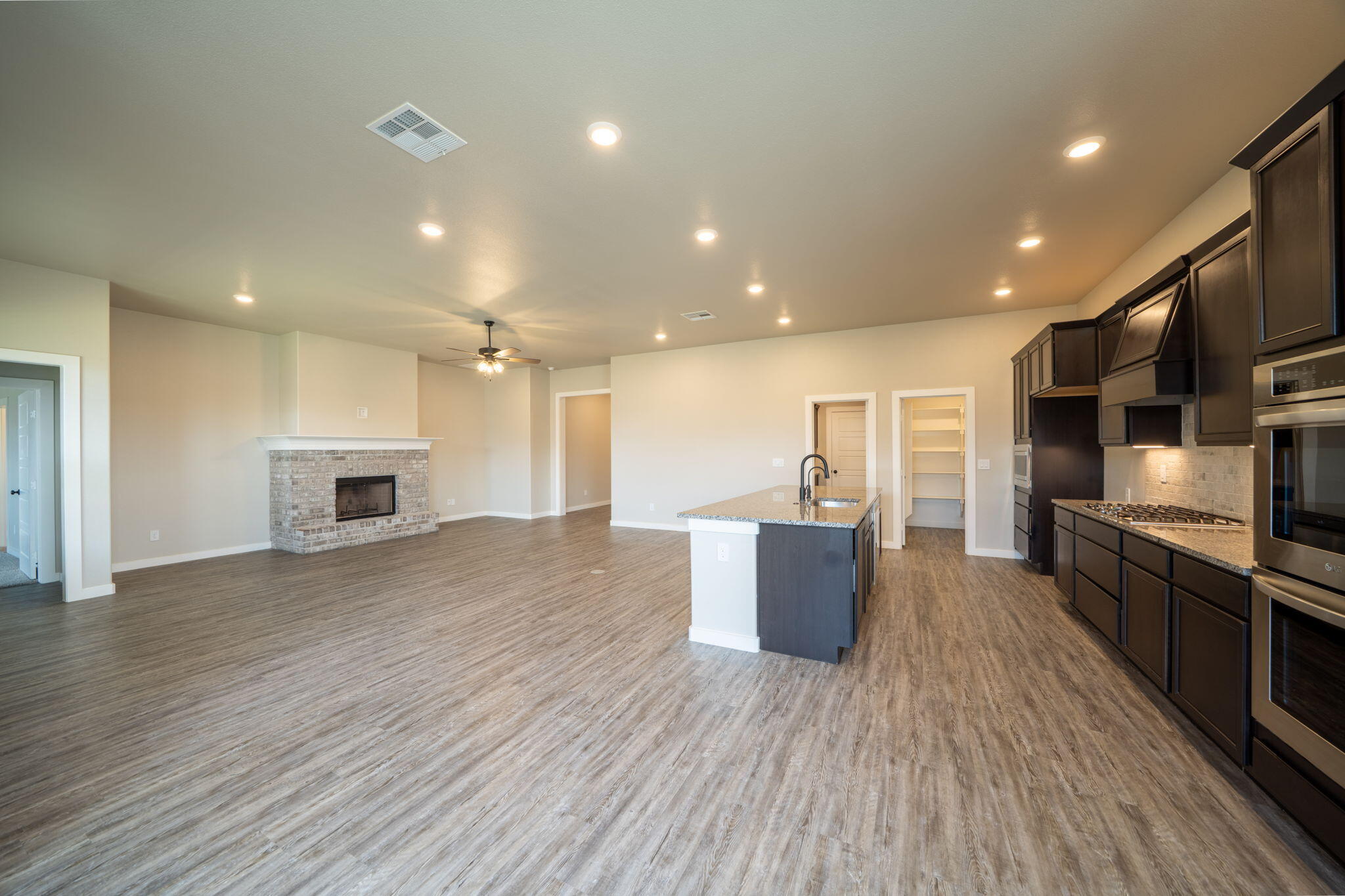 Open-plan kitchen and living area with dark cabinets, a central island, and a brick fireplace.