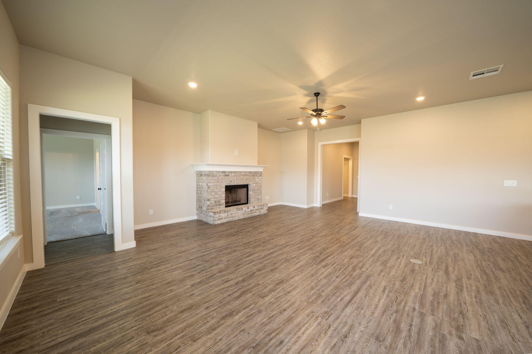 Vacant living room with a brick fireplace, wood-look flooring, and ceiling fan.