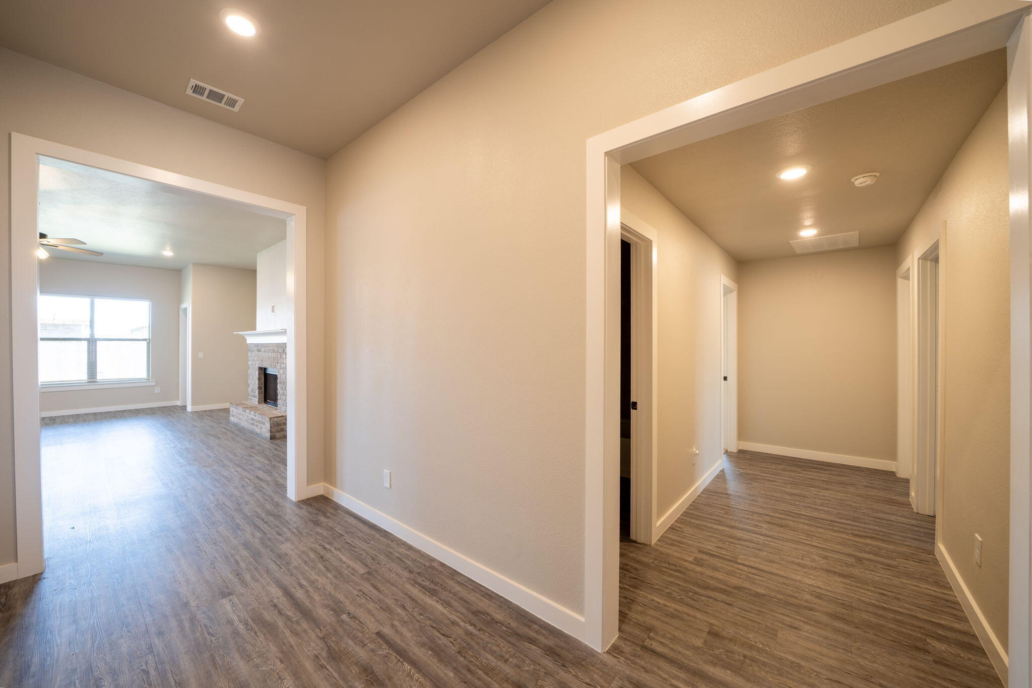 Hallway opening to a living room with a brick fireplace and wood-look floors.