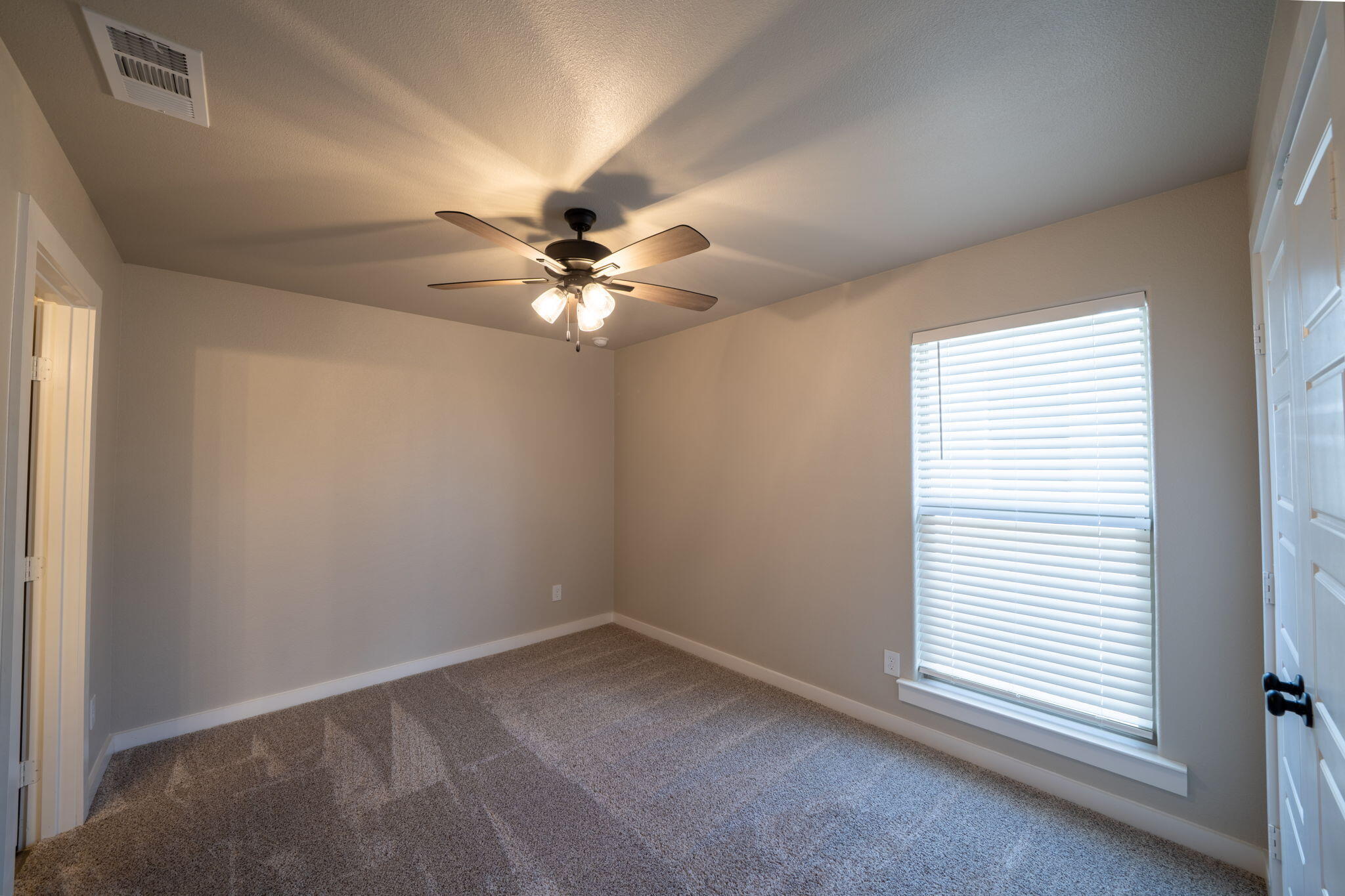 Empty bedroom with brown carpet, a ceiling fan, and a large window with white blinds.