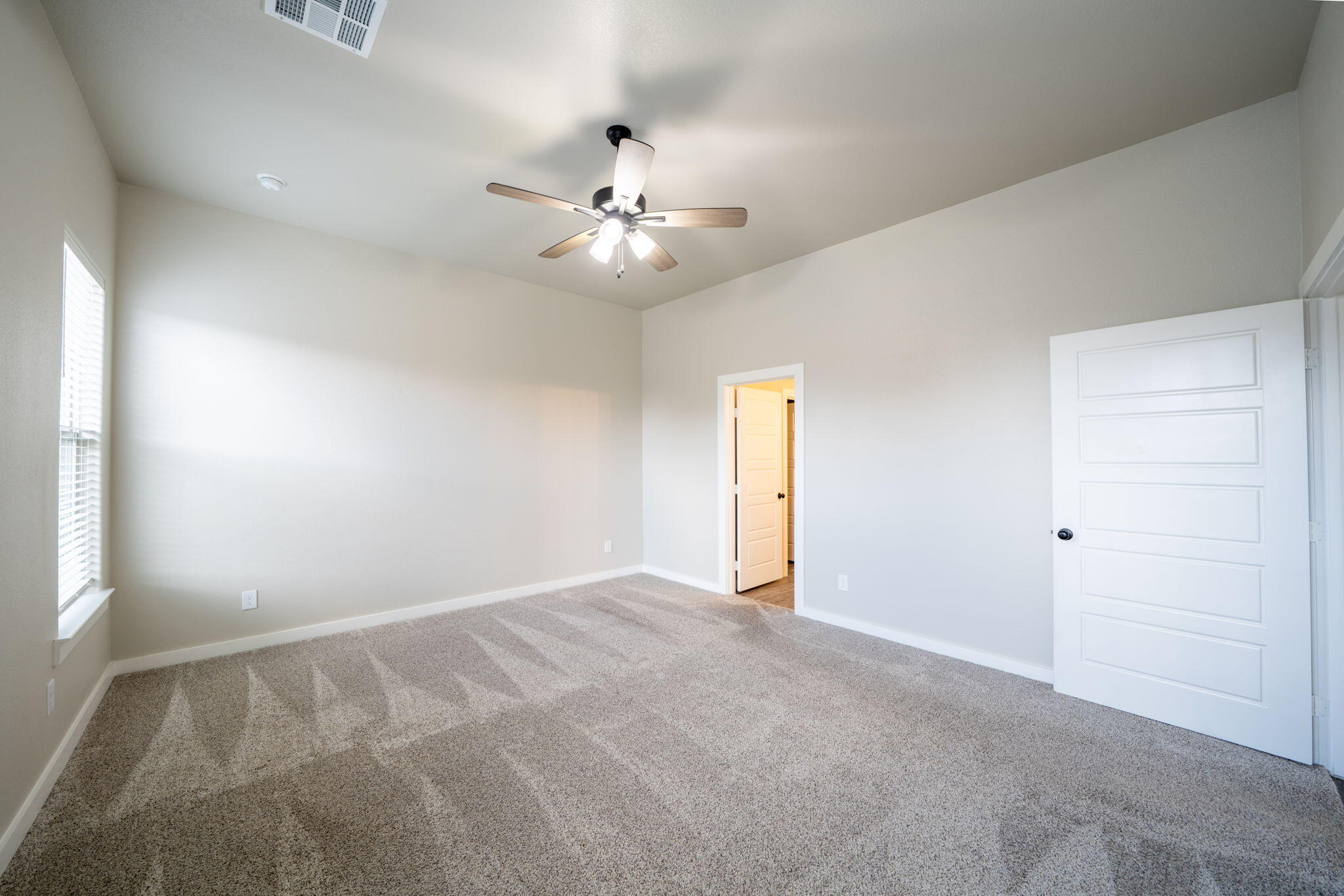 Empty bedroom with beige carpet, a ceiling fan, window blinds, and an open doorway.