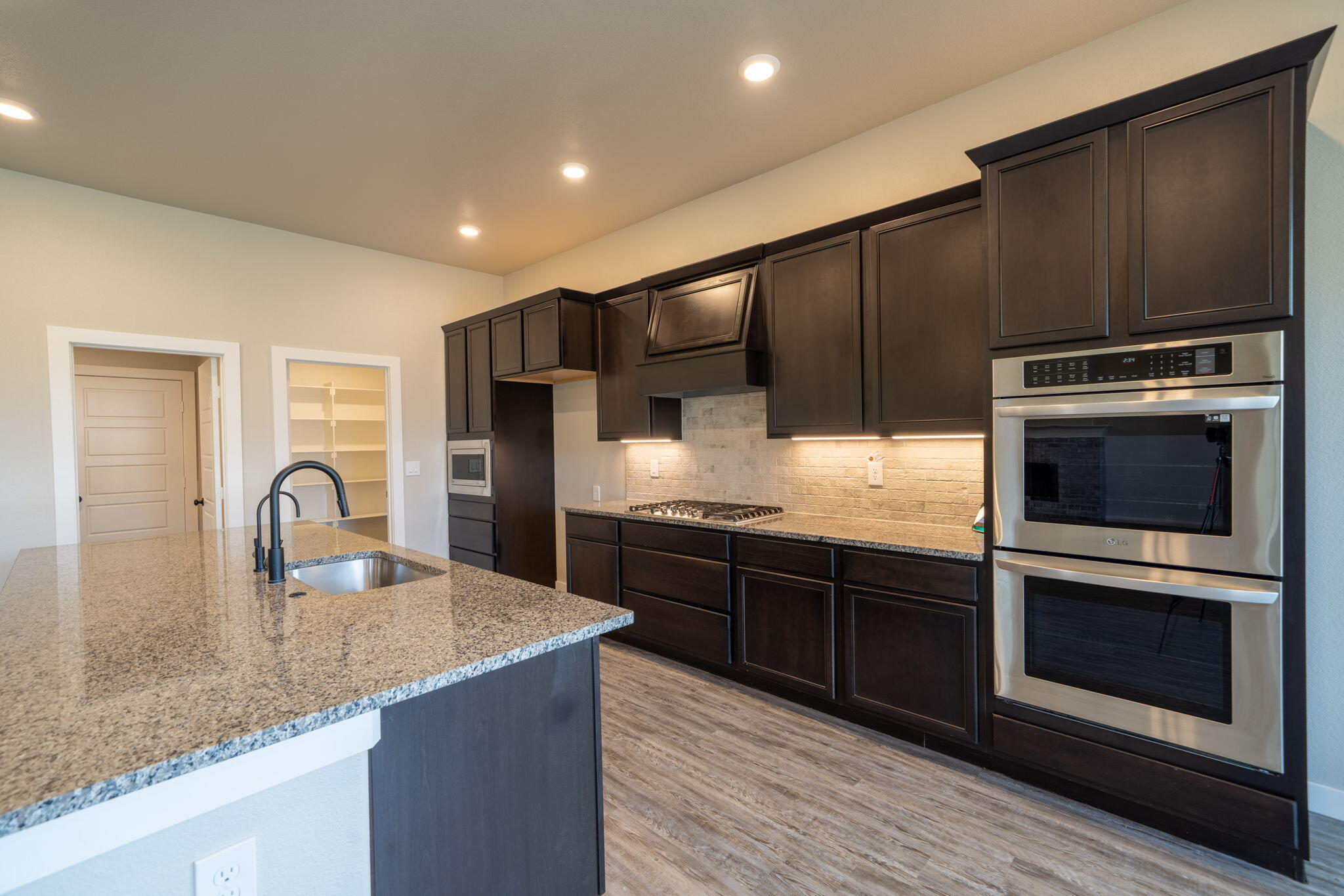 Modern kitchen with dark cabinetry, granite island, gas cooktop, and stainless steel double ovens.
