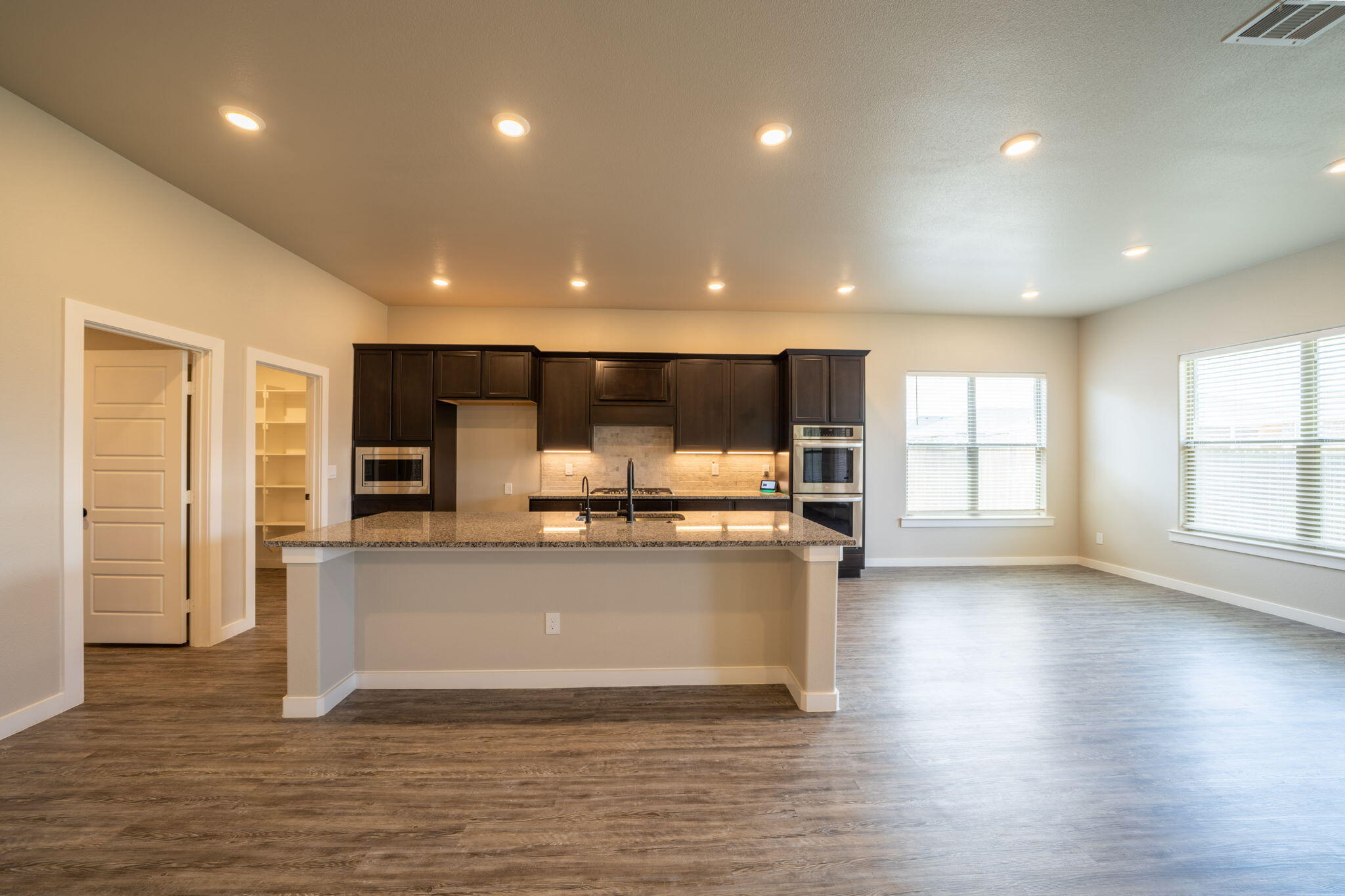 Kitchen with a large granite island, dark cabinets, and stainless steel appliances.