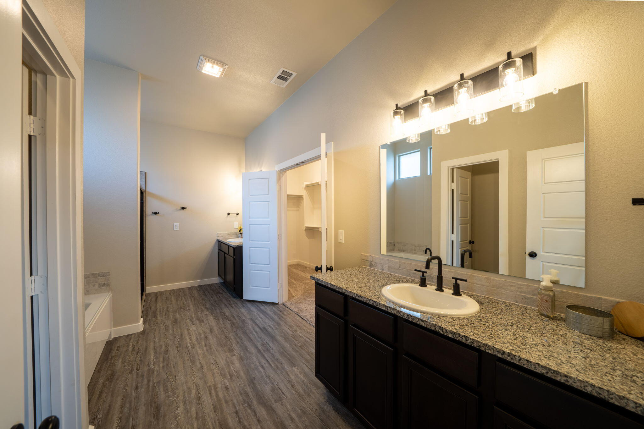 Bathroom with a long dark vanity, granite countertop, large mirror, and open walk-in closet doorway.