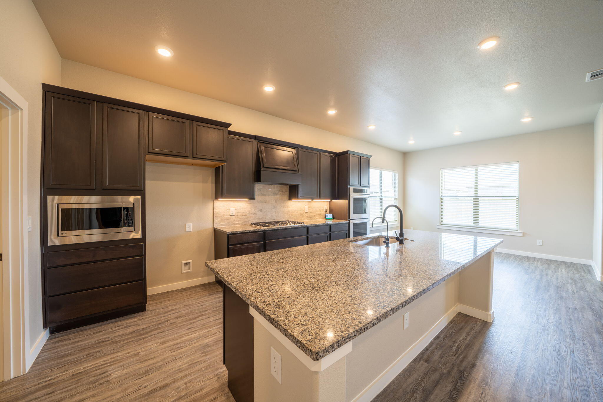 Kitchen with dark cabinets, granite island and sink, and built-in stainless steel appliances.