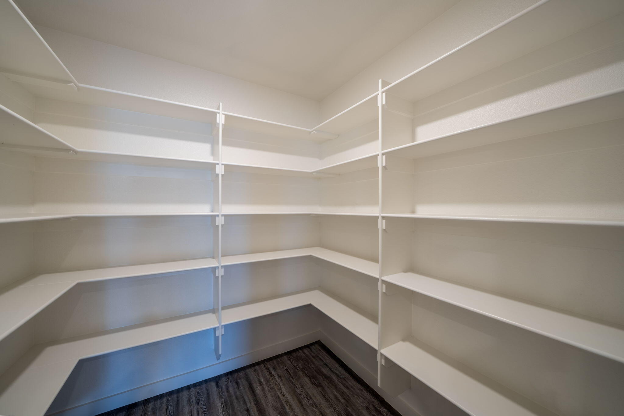 Walk-in closet with white wraparound shelves and dark wood-look flooring.