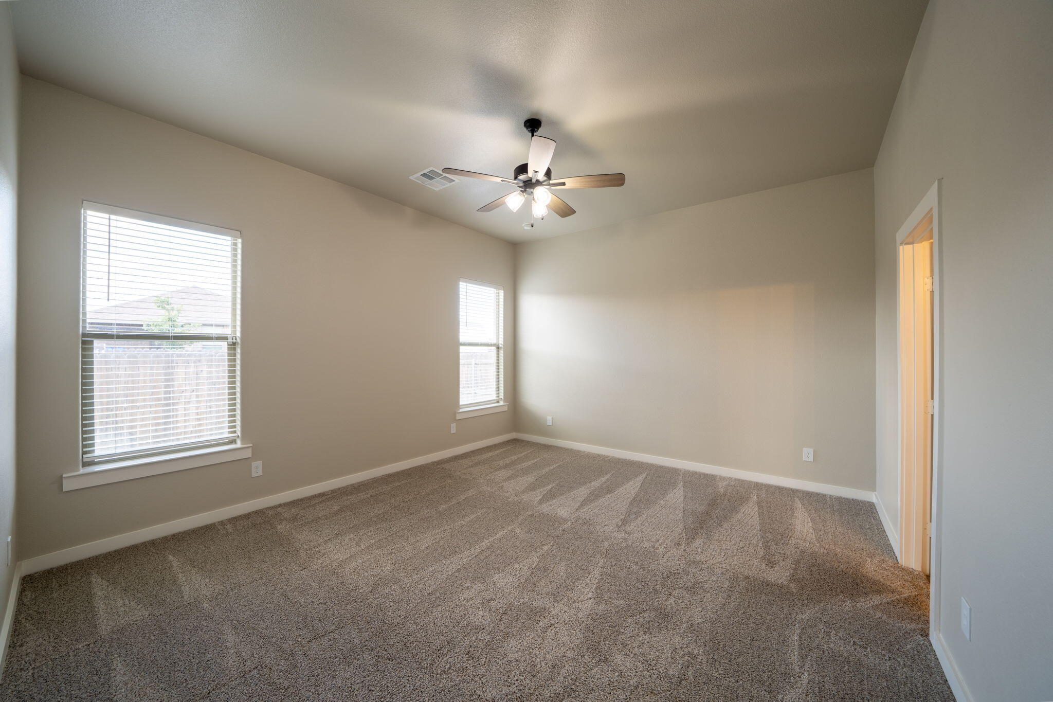 Empty bedroom with brown carpet, two windows, and a ceiling fan beneath a high ceiling.