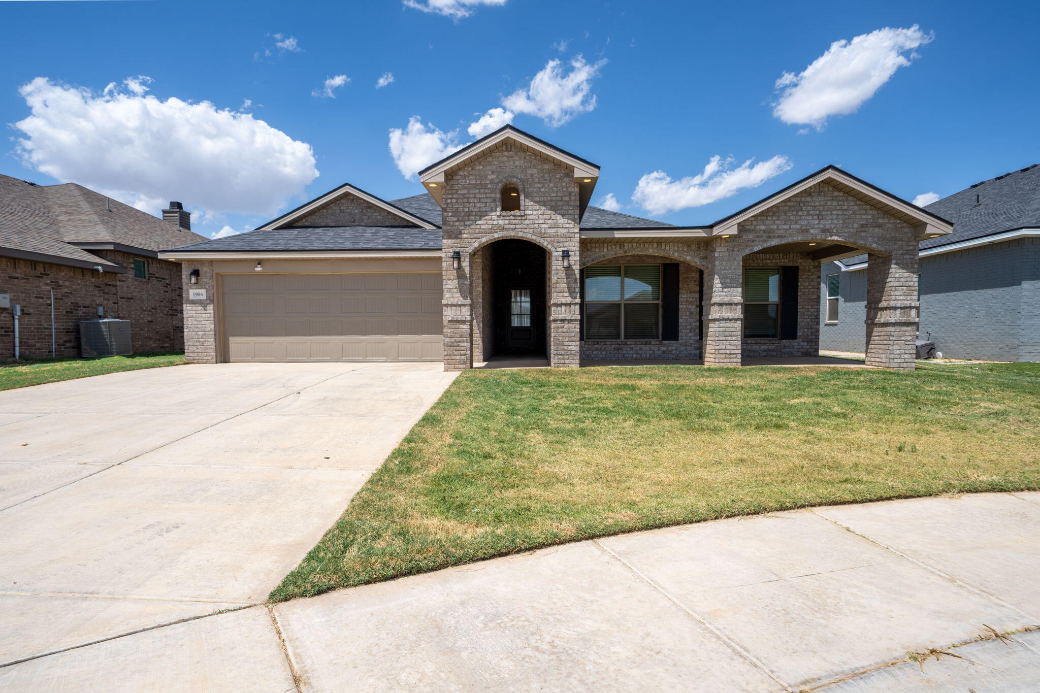 Brick house with a central arched entry, covered porch, two-car garage, and broad driveway.