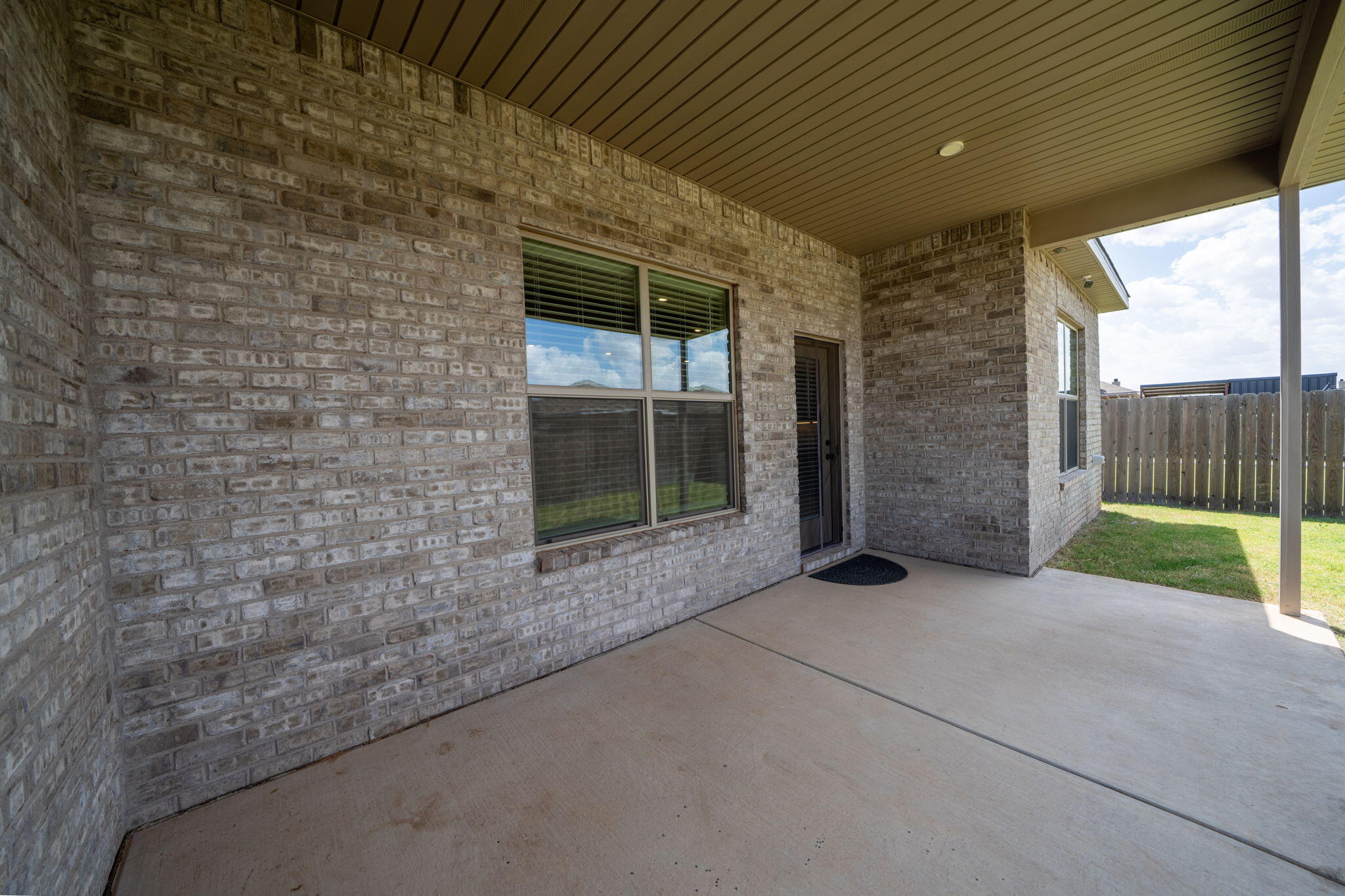 Covered brick patio with a concrete floor, windows, and a fenced backyard.