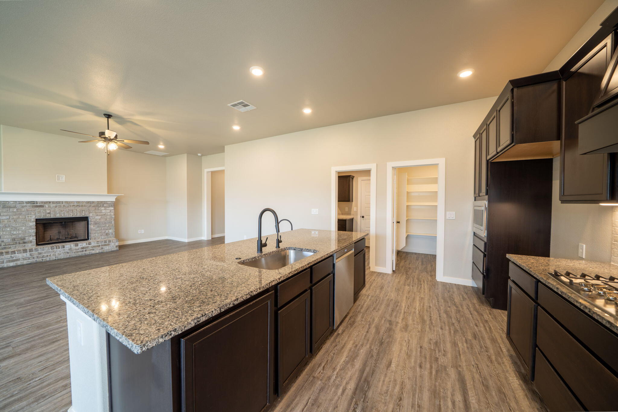 Kitchen with a large granite island, dark cabinets, and an adjoining living area with a brick fireplace.